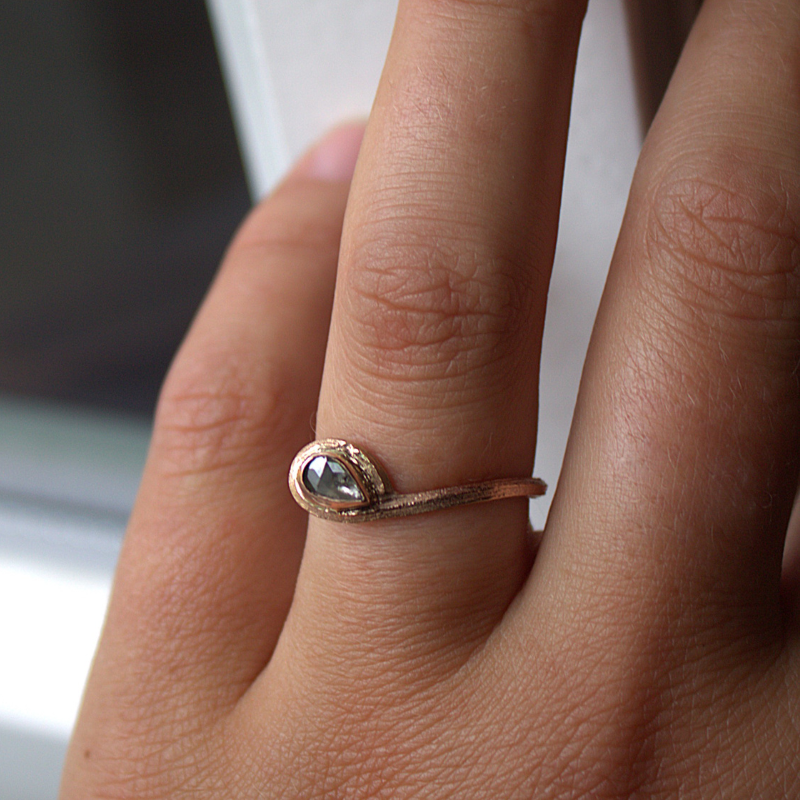 Goud en golvend bamboe eindigend in een loop waarin een roosgeslepen natuurlijk grijze diamant is gezet. Een a-symmetrisch organische elegante solitaire ring.