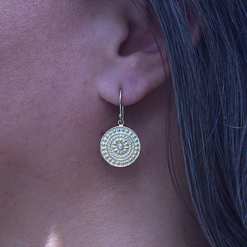 Gouden dragonstail munt/coin/schild met witte diamant aan een minimalistische oorhaak. Design en handgemaakt door Goudsmederij Goedbloed foto op model