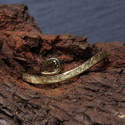 Gouden minimalistische golvende ring met een ijsmattering en in de golf een peervormige facetgeslepen bruine diamant. Eigentijds ontwerp door Goudsmederij Goedbloed