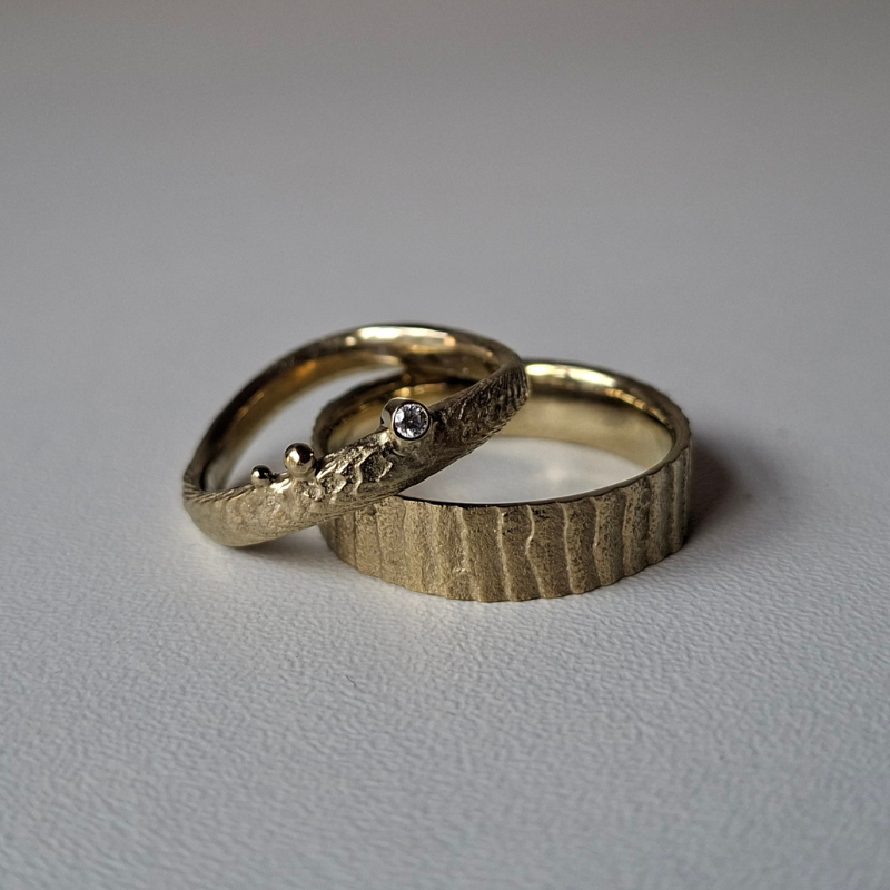 Handgemaakt gouden organisch trouwringen met een design geïnspireerd door de zee handgemaakt. de damesring heeft een golvend band en is verfijnd met een witte diamant, de herenring is met dezelfde textuur, maar heeft een brede strakke band. In het atelier van Goudsmederij Goedbloed gemaakt.