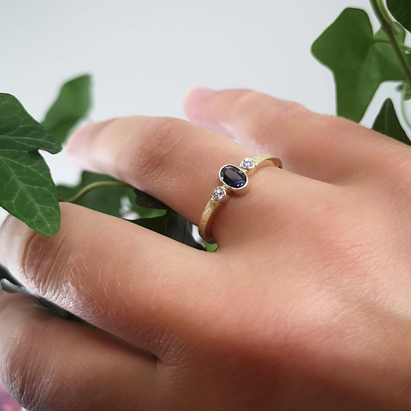 Klassiek verlovingsring aanzoekring symmetisch design met witte diamanten en ovaal facetgeslepen Ioliet als middensteen. Modern afwerking met een ijsmattering. Handgemaakt door Goudsmederij Goedbloed. Op model