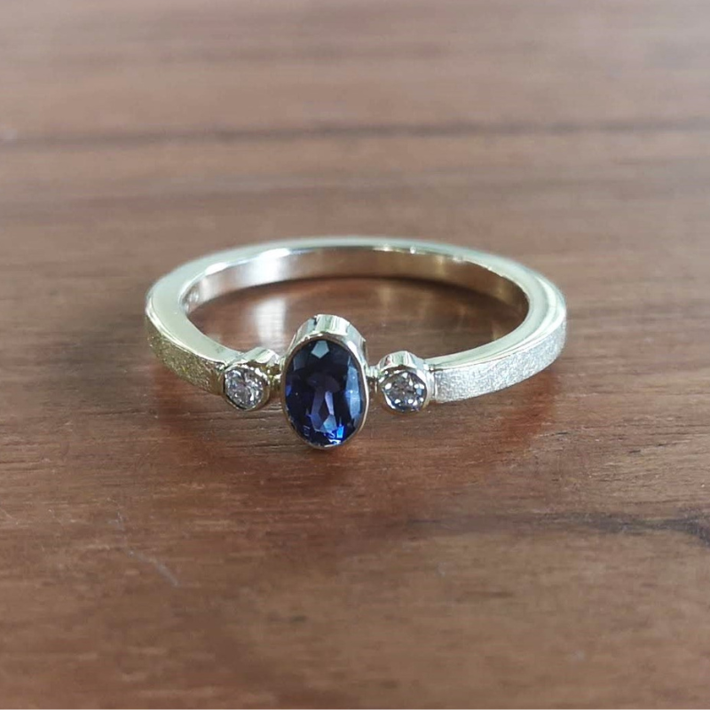 Klassiek verlovingsring aanzoekring symmetisch design met witte diamanten en ovaal facetgeslepen Ioliet als middensteen. Modern afwerking met een ijsmattering. Handgemaakt door Goudsmederij Goedbloed