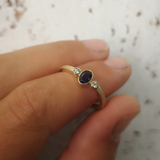 Klassiek verlovingsring aanzoekring symmetisch design met witte diamanten en ovaal facetgeslepen Ioliet als middensteen. Modern afwerking met een ijsmattering. Handgemaakt door Goudsmederij Goedbloed.