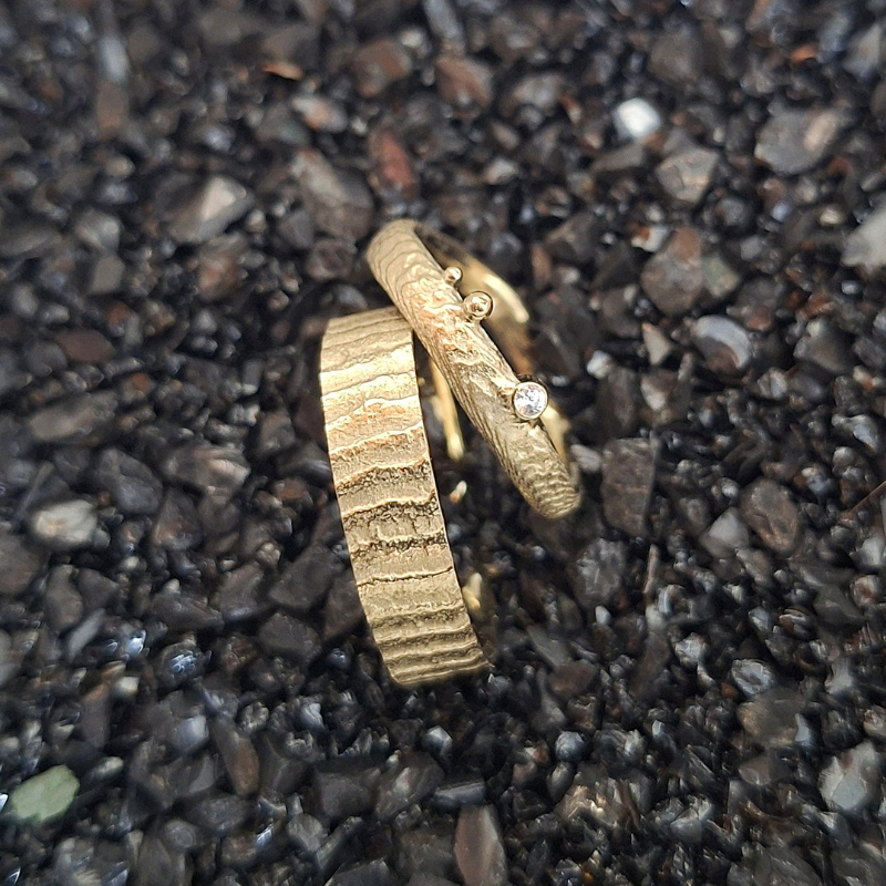Handgemaakt gouden organisch trouwringen met een design geïnspireerd door de zee handgemaakt. de damesring heeft een golvend band en is verfijnd met een witte diamant, de herenring is met dezelfde textuur, maar heeft een brede strakke band. In het atelier van Goudsmederij Goedbloed gemaakt.