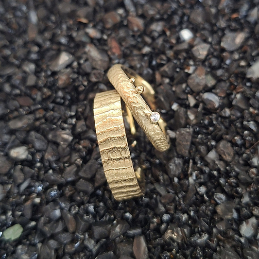Handgemaakt gouden organisch trouwringen met een design geïnspireerd door de zee handgemaakt. de damesring heeft een golvend band en is verfijnd met een witte diamant, de herenring is met dezelfde textuur, maar heeft een brede strakke band. In het atelier van Goudsmederij Goedbloed gemaakt.