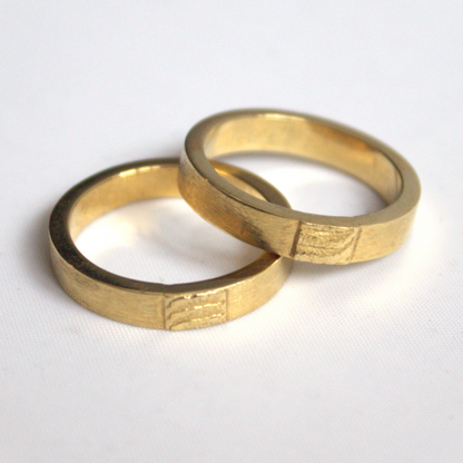 Klassieke trouwringen met een zandgegoten imprint van de zee als tussenstuk minimalistisch handgemaakt door Goudsmederij Goedbloed