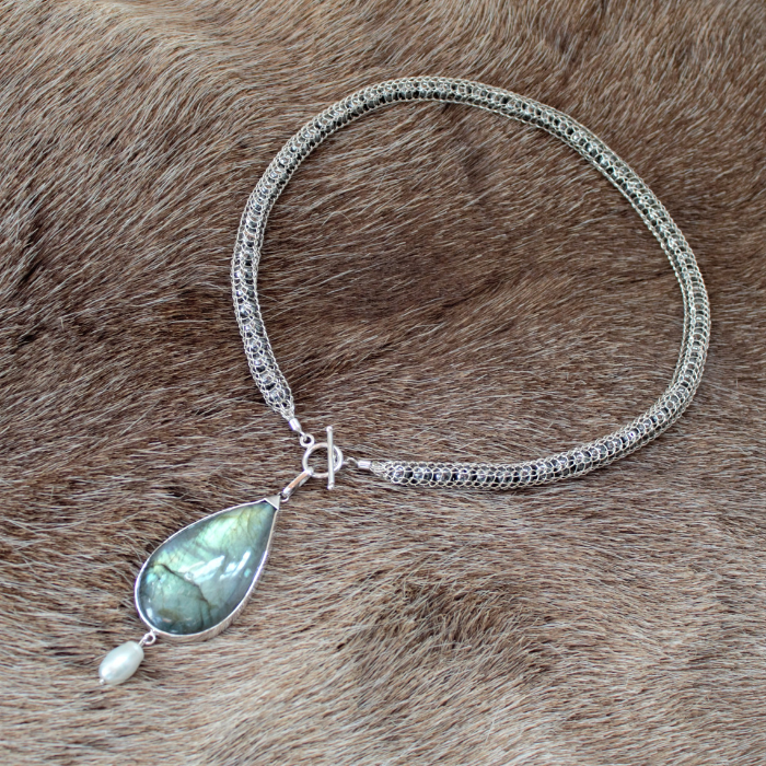 Van zilverdraad handgeweven collier opgevuld met hematiet en een hanger met een peervormige Labradoriet waaronder speels een witte barokparel hangt. Handgemaakt volgens oude smeedtechnieken door Goudsmederij Goedbloed